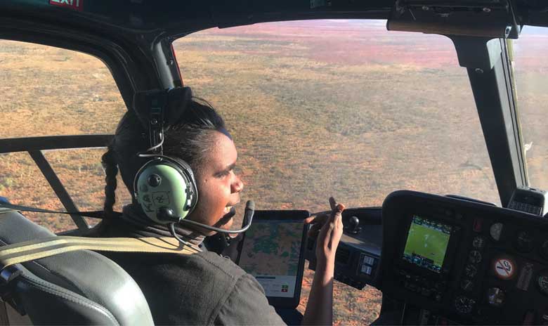 Ngurrara senior ranger, Sumayah Surprise, navigating a helicopter overlooking bushlands