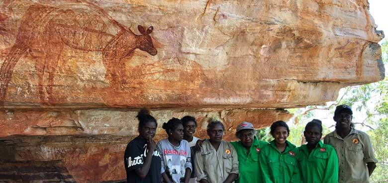 Indigenous rangers standing with school students recording a rock art site