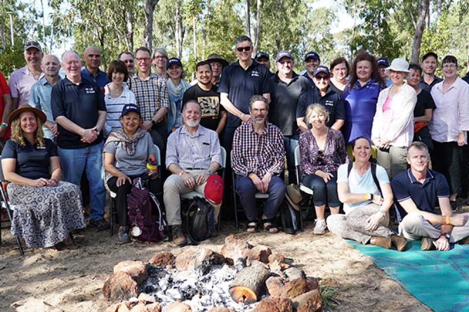 A group of 31 people sit or stand. In the foreground is a campfire.